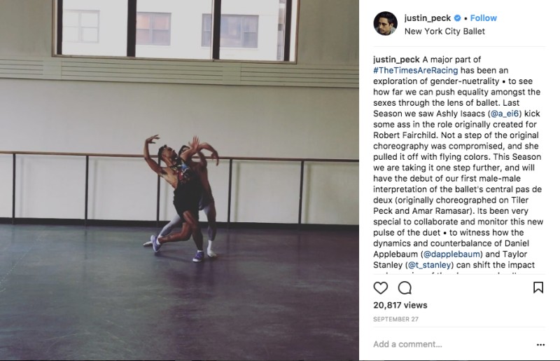 A studio shot from Justin Peck's Instagram page. Two male dancers stand hear one another in dramatic poses. Their arms create curved cyclical shapes. They wear tank tops, shorts and sneakers.